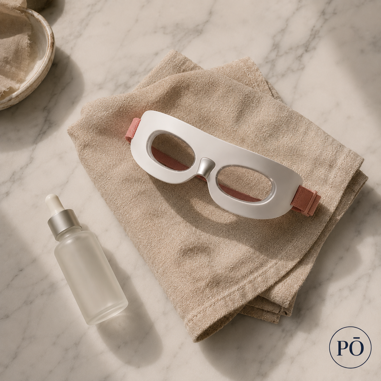 PHŌRMA Vista Light eye mask laid on a linen cloth next to a facial serum, marble surface